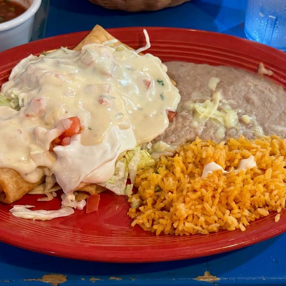 Mexican-style plate with cheese-covered enchiladas, refried beans, orange rice, lettuce, and salsa on a red platter.