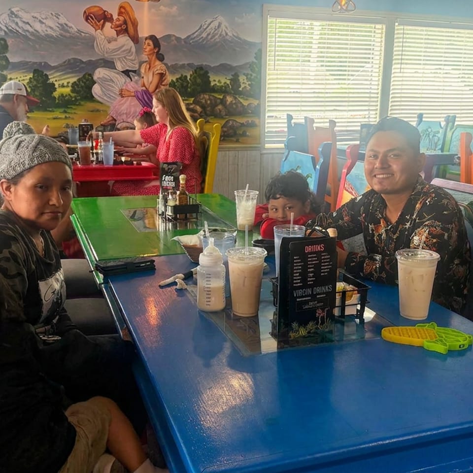 Family enjoying drinks at a colorful restaurant table surrounded by vibrant chairs, murals, and children’s play area.