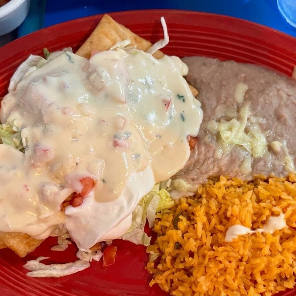 Mexican combination plate with cheesy enchiladas, refried beans, Spanish rice, shredded lettuce, and tortilla chips on a red platter.