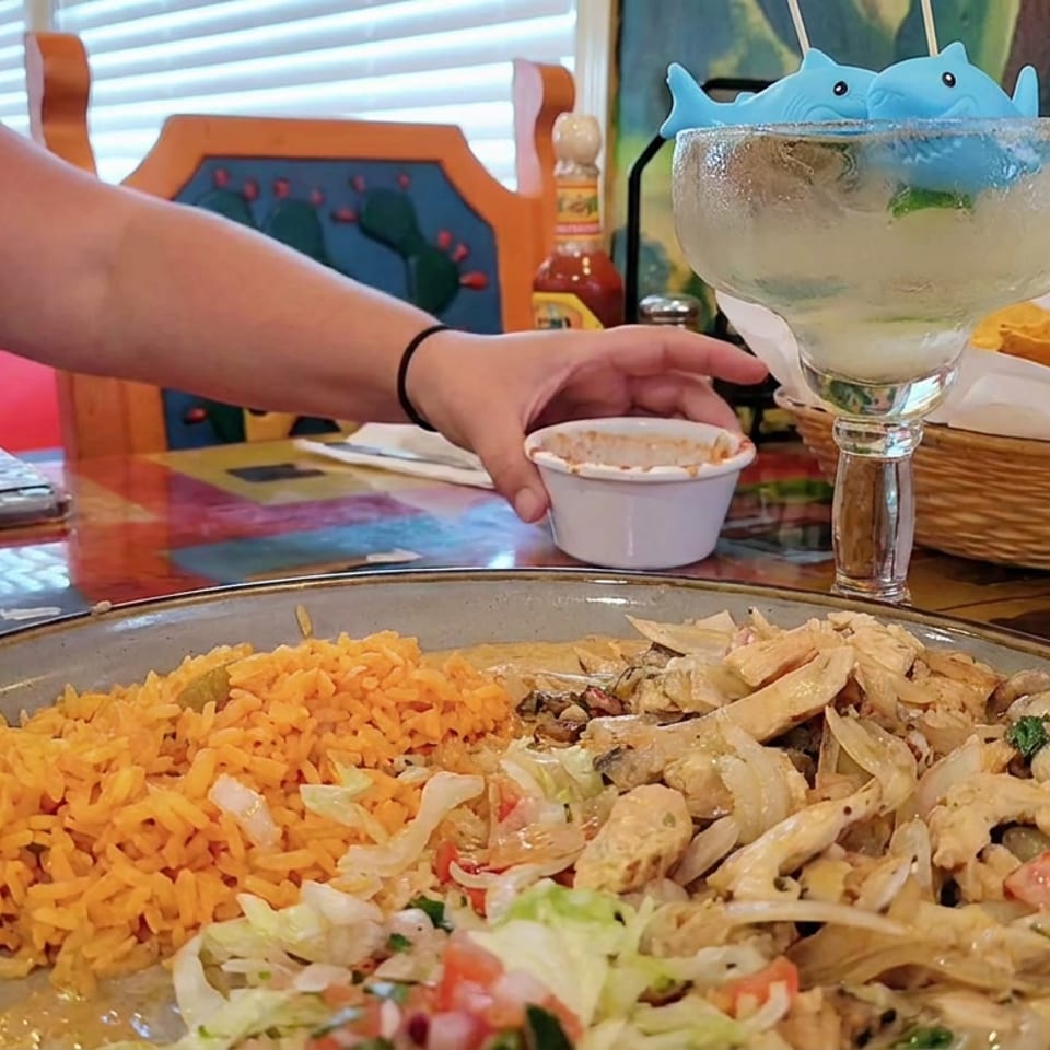 Mexican restaurant table featuring orange rice, creamy chicken fajitas, tortilla chips, salsa, and oversized margaritas.